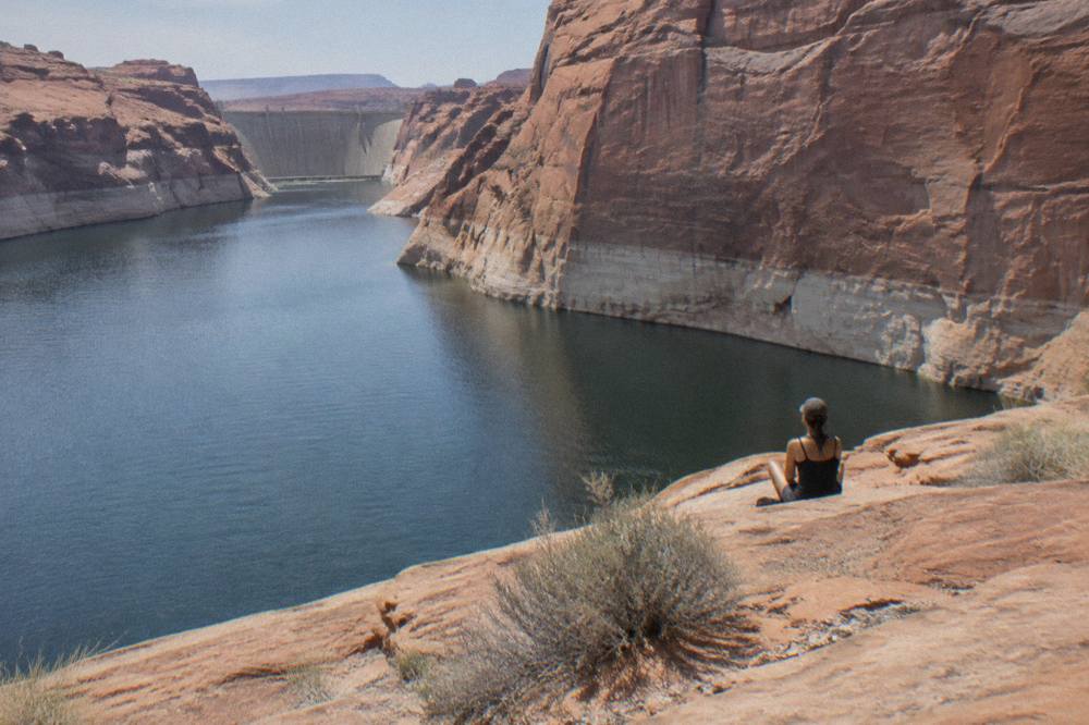 Wide view of the calm Colorado River curving around a tall sandstone cliff below Glen Canyon Dam